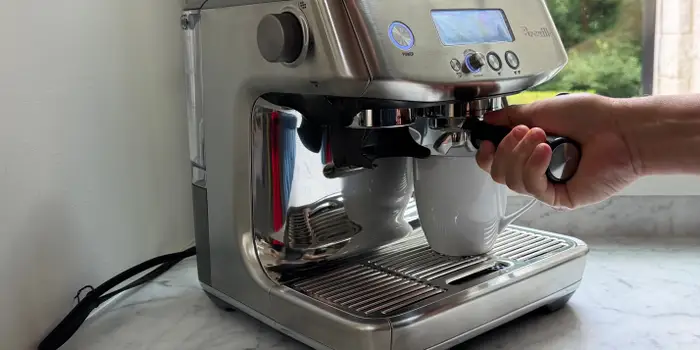 Hand locking a portafilter into a Breville espresso machine on a kitchen counter