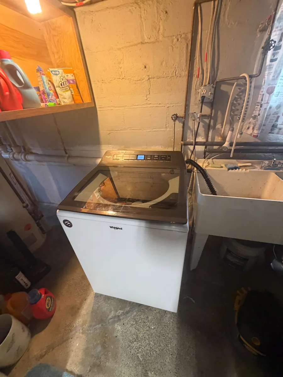 Whirlpool top-load washer beside a utility sink in a basement laundry